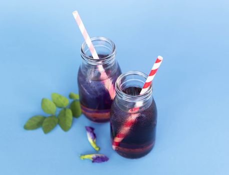 Butterfly pea juce in grass bottle with leaf and flower on light blue background, herb dink for healthy concept