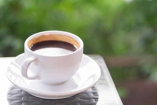 Closeup hot americano coffee on glass table with green nature background