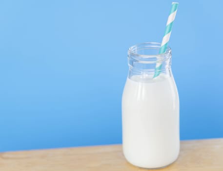 Bottle of fresh milk with straw on light blue background, food healthy concept