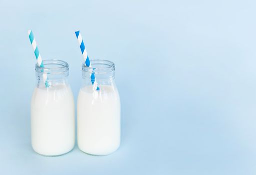 Bottle of fresh milk with straw on light blue background, food healthy concept