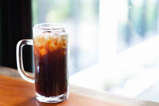 Closeup glass of ice americano coffee on wood table with green nature background, selective focus