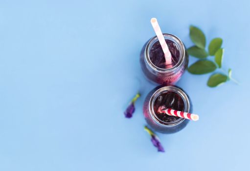 Butterfly pea juce in grass bottle with leaf and flower on light blue background, herb dink for healthy concept