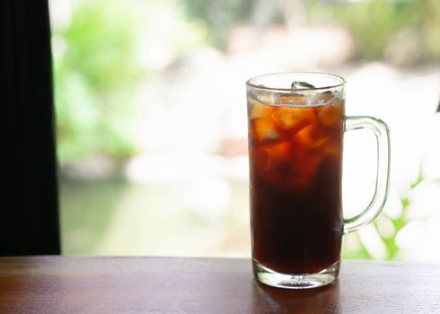 Closeup glass of ice americano coffee with green nature background, selective focus