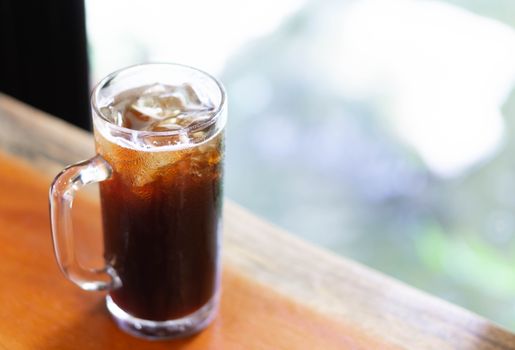 Closeup glass of ice americano coffee on wood table with green nature background, selective focus