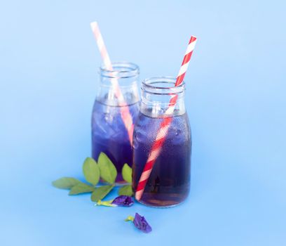 Butterfly pea juce in grass bottle with leaf and flower on light blue background, herb dink for healthy concept