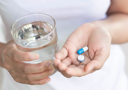 Closeup woman hand holding pills and glass of water, health care and medical concept, selective focus