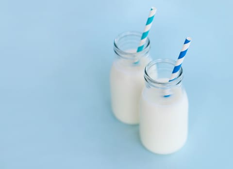 Bottle of fresh milk with straw on light blue background, food healthy concept