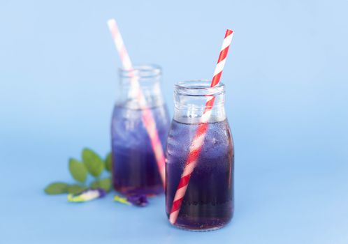 Butterfly pea juce in grass bottle with leaf and flower on light blue background, herb dink for healthy concept