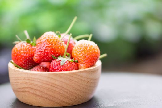 Closeup red strawberry in wood bowl with green nature background, selective focus