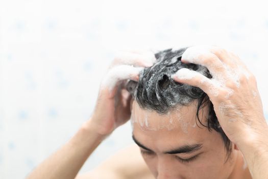 Closeup young man washing hair with with shampoo in the bathroom, health care concept, selective focus 