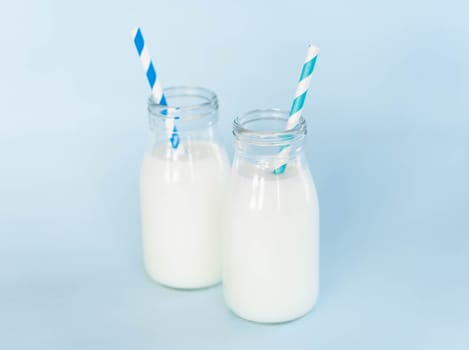 Bottle of fresh milk with straw on light blue background, food healthy concept