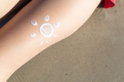 Closeup woman applying sun screen lotion on her legs with draw sun symbol on the beach, Holiday and relax concept