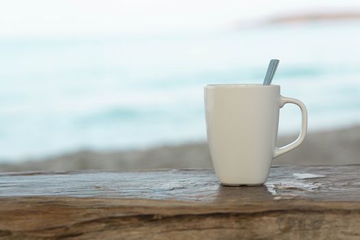 Closeup white ceramic glass of coffee on wood table with sea water and beach background