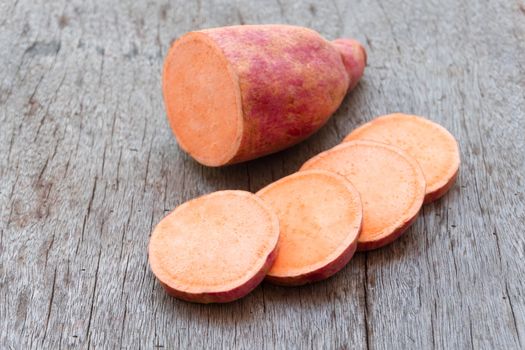 Sweet potato with slices on wooden background, raw food 