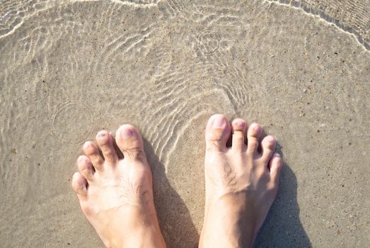 Closeup man feet standing on sea sand with relaxing time feeling in the holiday