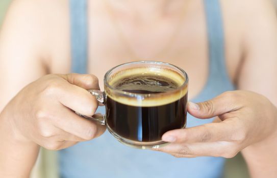 Closeup woman hand holding glass of hot americano coffee, selective focus, vintage tone