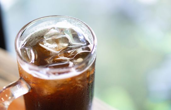 Closeup glass of ice americano coffee on wood table with green nature background, selective focus