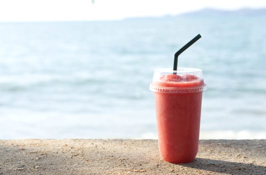 Closeup glass of strawberry smoothie with lignt in the morning and sea water background, Holiday and relax time