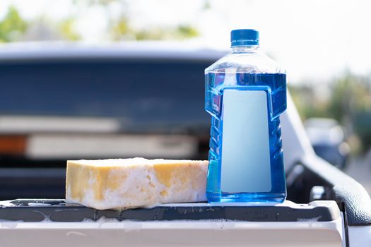 Close up bottle of car wash soap with yellow sponge for washing, selective focus