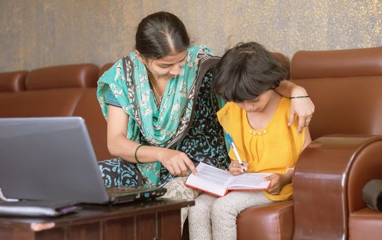 young mother teaching her child while working on laptop - concept of People Lifestyles and technology, work form home or wfh reality.