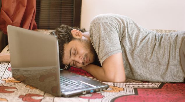 Tired young man sleeping in bed with laptop - hard work, laziness of working from home or WFH during coronavirus or covid-19 lock down concept