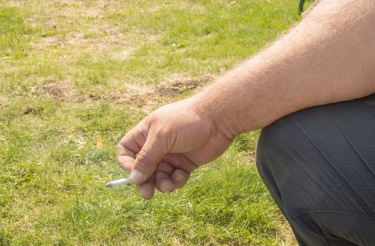 Close-up of an elderly man's hand holding a cigarette and Smoking against an open nature bokeh. Concept of harm of Smoking, Smoking cessation.