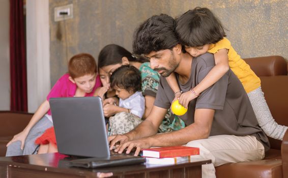 Children or kid playing by riding on father back and disturbing while father busy in working on laptop - Concept of work from home or WFH during covid-19 or coronavirus pandemic