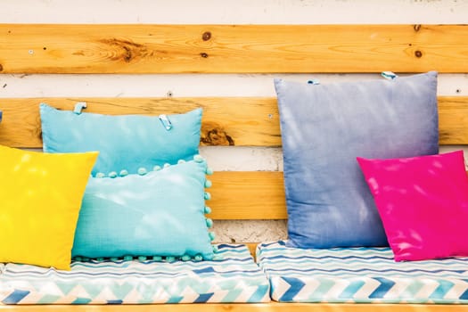 Close up pillows on an outdoor patio chair, with a blue striped cushioned bench.