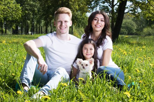 Happy smiling family of parents and daughter with pet dog in summer park