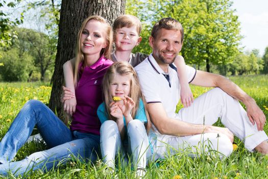 Happy family of parents and two children sitting on grass in spring park