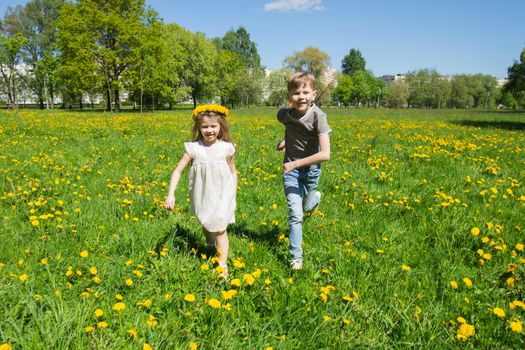 Young boy and girl brither and sister running in a sunny meadow with dandelion flowers family fun concept