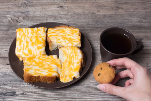 A Cup of coffee with fresh toast, melted cheese and cupcake in hand on a wooden background. Morning diet Breakfast. Proper diet.