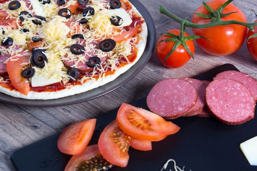 Cooking pizza at home. Pizza with tomatoes, olives and cheese is on the plate. Ingredients for cooking pizza are on a wooden table