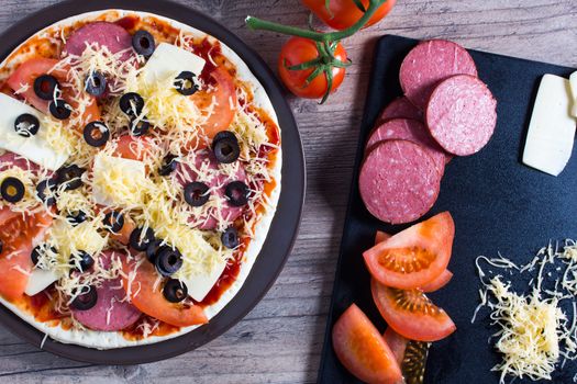Pizza with tomatoes, olives and cheese is on the plate. Ingredients for cooking pizza are on a wooden table. Cooking pizza at home