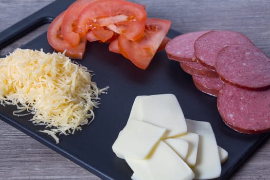 Tomatoes, sausage and cheese are on the cutting Board on the kitchen table. We cook at home