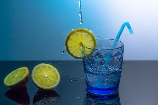 Splashes of water fall into a glass with lemon and ice.A mug of ice and water sits on a mirrored table with sliced lemons.Preparation of a fresh drink tonic,juice or cocktail.Water splash,water drop