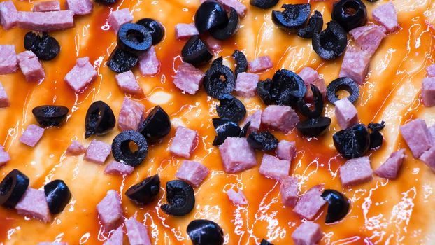 Ingredients on raw pizza close-up.Olives and sliced sausage lie on a pizza dough anointed with tomato paste. Cooking pizza at home.