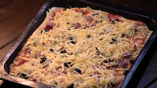 We prepare pizza at home from olives, sausage, tomato paste and cheese. Raw pizza is on a baking sheet in the oven. The recipe of the yummy pizza