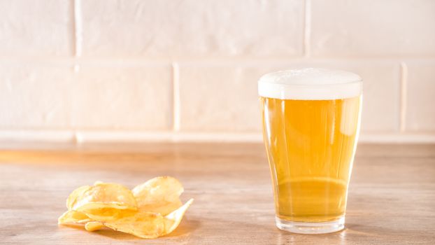 Fresh foamy beer with chips lying on a wooden table in the morning sun.