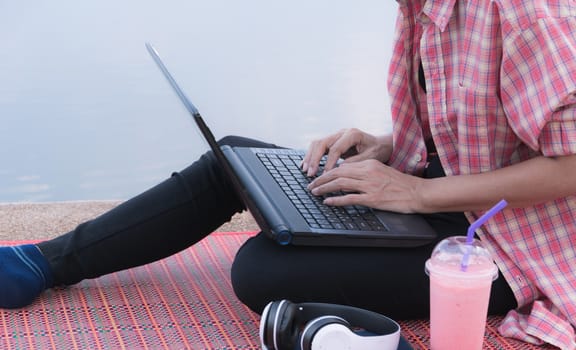 A woman using laptop computer while sitting beside river.