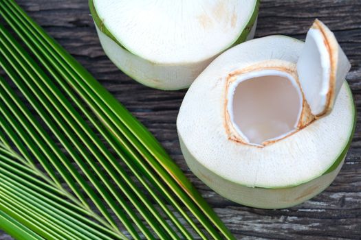 Fresh organic coconut water with coconut leaves on wooden table.