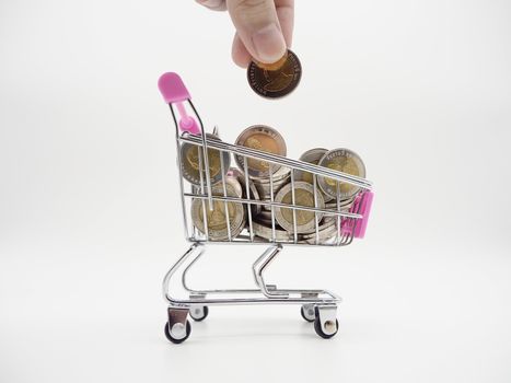 Hand holding a coin with pile of coin in the shopping cart on white and grey background