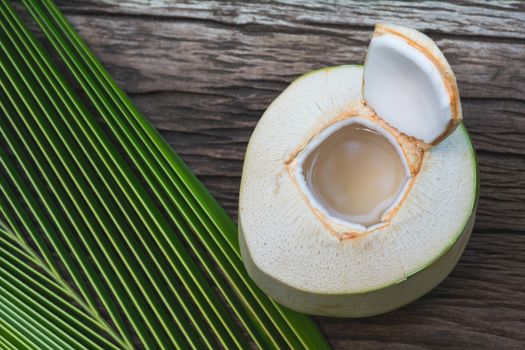 Fresh organic coconut water with coconut leaves on wooden table.