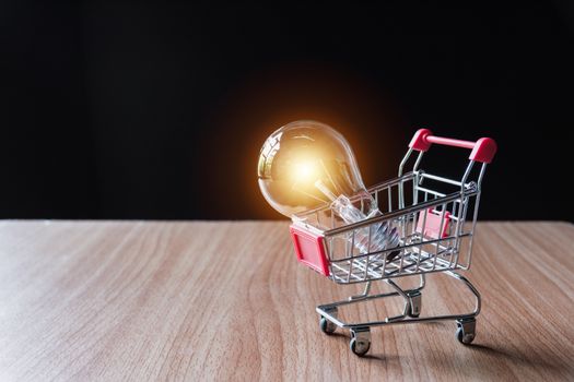 Energy saving light bulb with stacks of coins and shopping cart for saving, financial and shopping concept.