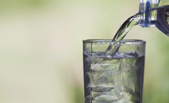 Female hand pouring water from bottle to glass on blur background