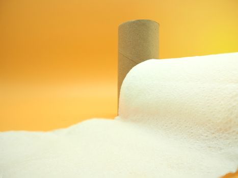 A tissue paper with roll core. Empty roll with toilet paper on a orange background.