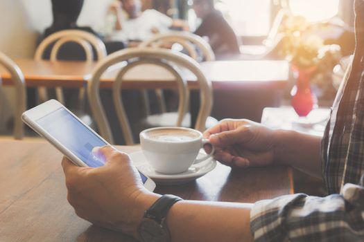 Male using a smart phone with coffee cup on wooden table.