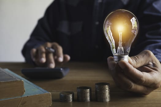 Hand of male holding a light bulb with stack of coins for accounting and creative concept.