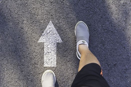Top view of man wearing white shoes choosing a way marked with white arrows. Chooses the right path concept.