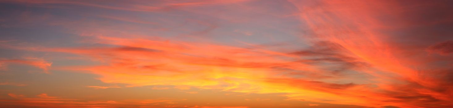 Beautiful high resolution panorama of orange and red sunset clouds in the evening sky.